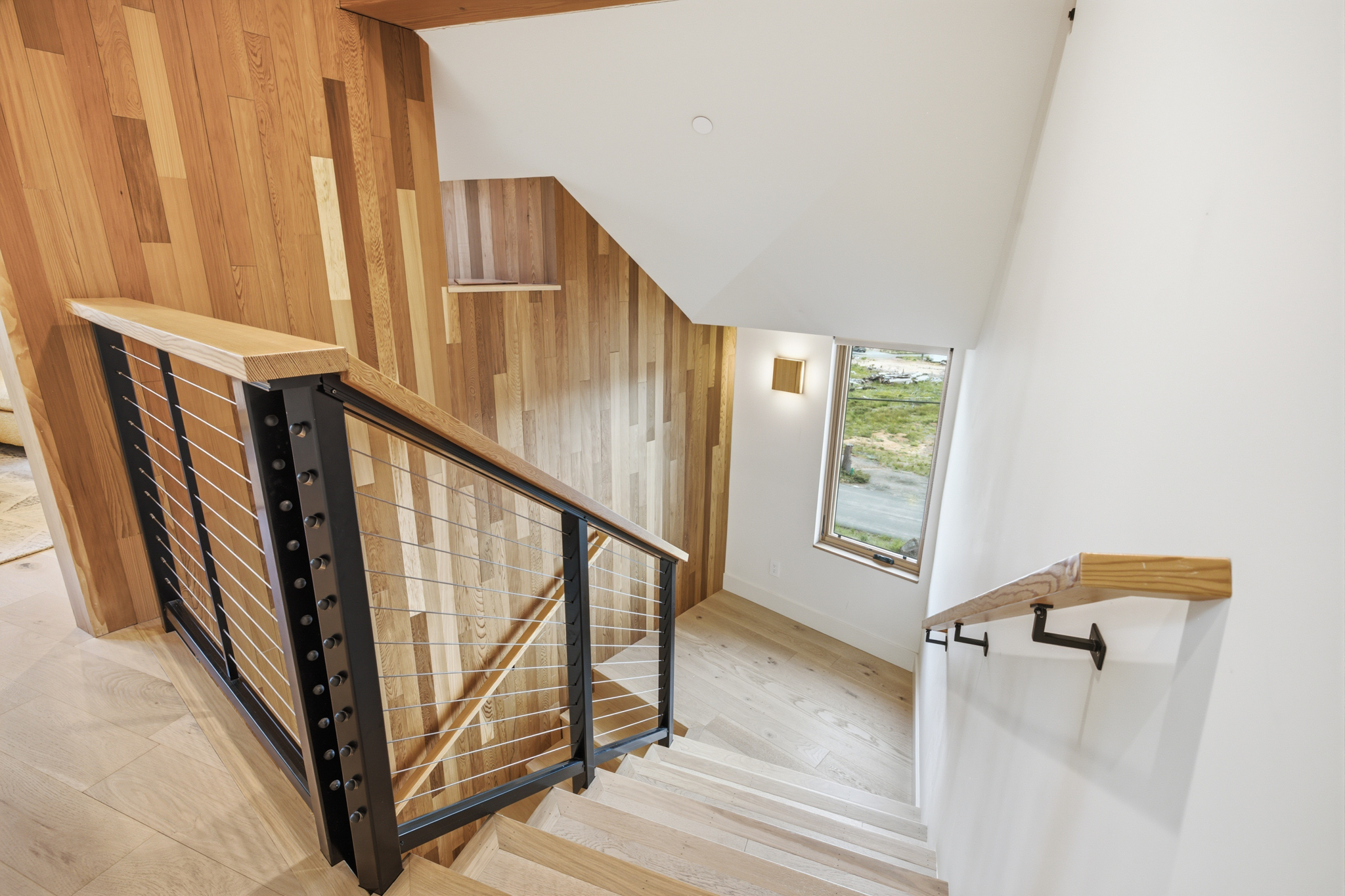 Open staircase with black cable railing and wood accent wall