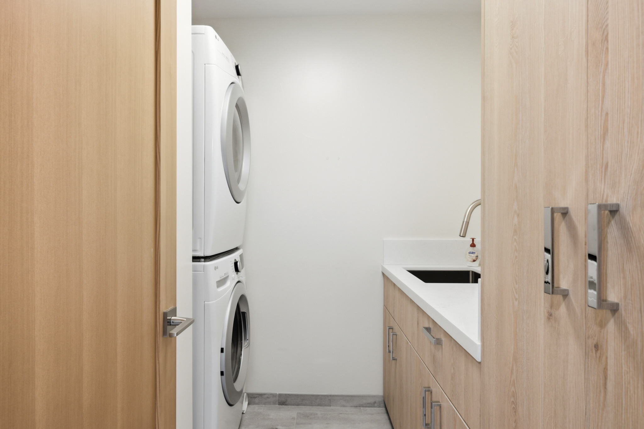 Laundry room with stacked washer, dryer, sink, and wood cabinets